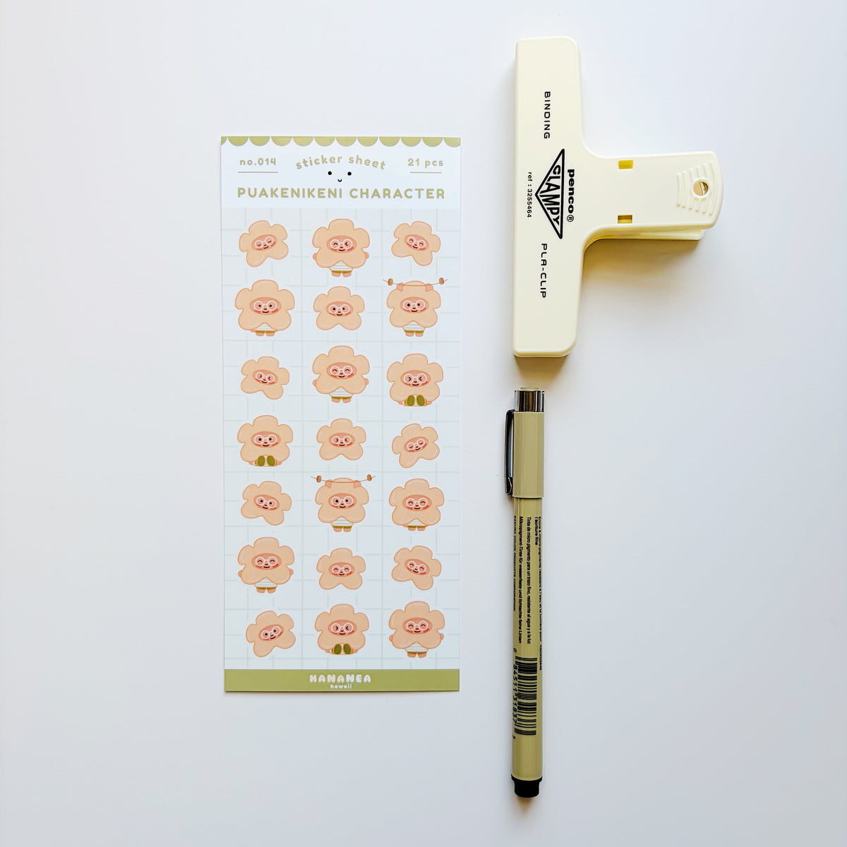 A sheet of cute pink cartoon character stickers labeled 'PUAKENIKENI CHARACTER' arranged on a white background next to a cream-colored plastic clip and a beige pen.