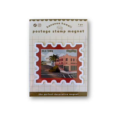 A postage stamp-shaped decorative magnet, featuring a red stamp border and a central illustrated scene of a tropical town with palm trees and buildings.