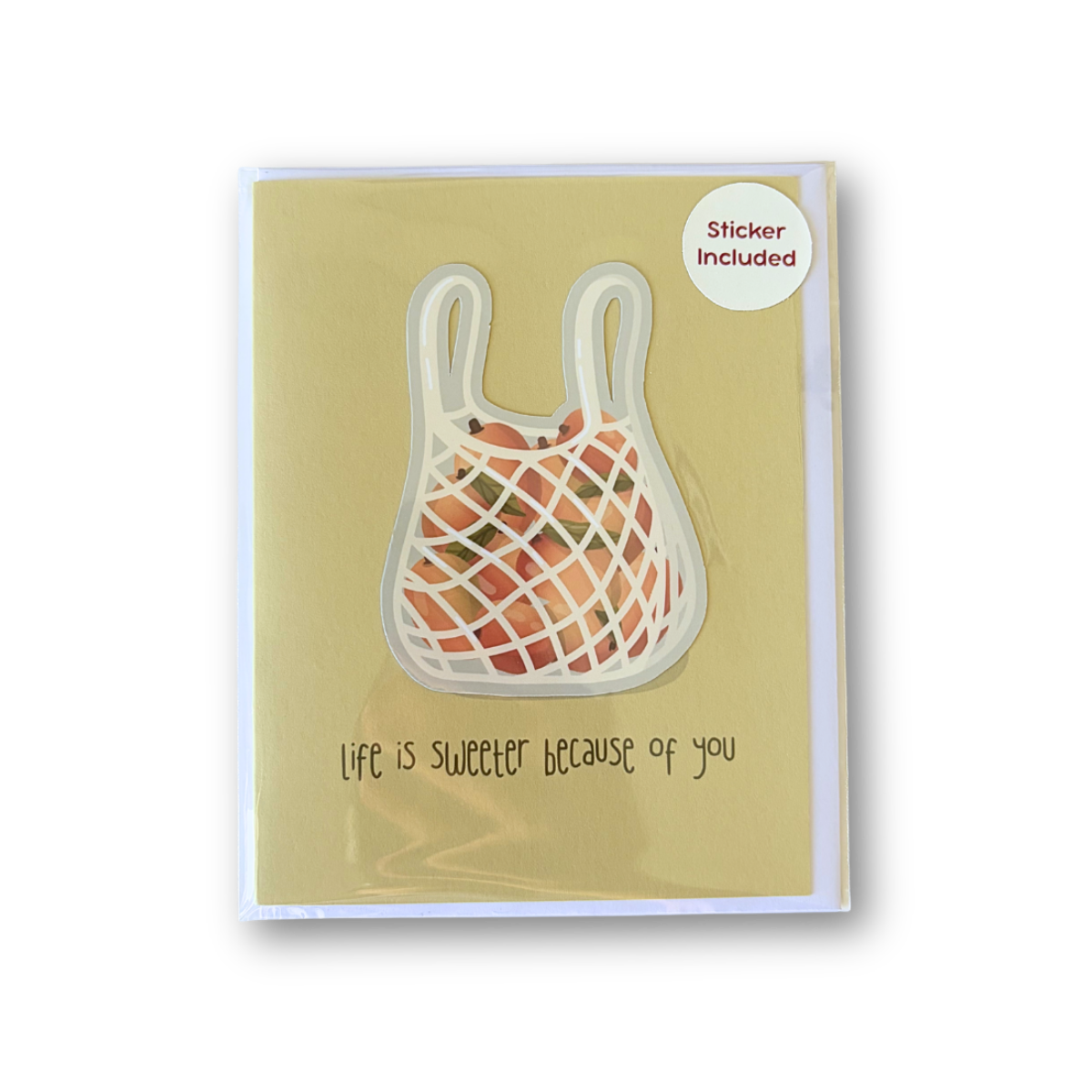 A greeting card with a yellow-green background featuring a netted shopping bag illustration and the handwritten text 'Life is sweeter because of you'. A small white circle in the top right says 'Sticker Included'.