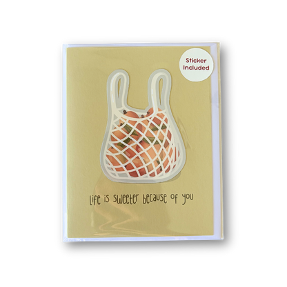 A greeting card with a yellow-green background featuring a netted shopping bag illustration and the handwritten text 'Life is sweeter because of you'. A small white circle in the top right says 'Sticker Included'.