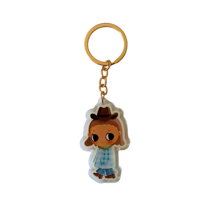 A cartoon-style acrylic keychain featuring a character with brown hair, a brown hat, a blue plaid shirt, and blue pants, attached to a gold metal key ring and chain on a white background.