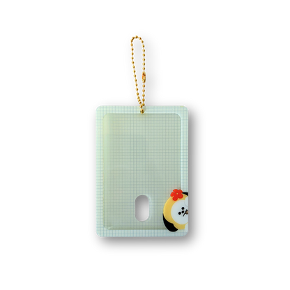 A rectangular translucent pale green card holder or phone case with a small oval cutout, a gold-and-white hanging loop, and a small cartoon character printed near the lower right corner, shown on a plain white background.