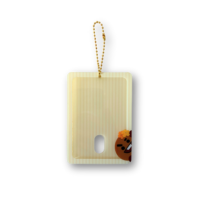 A pale yellow translucent rectangular card holder or phone case with a gold bead strap, featuring a small cartoon character printed near the bottom right corner.
