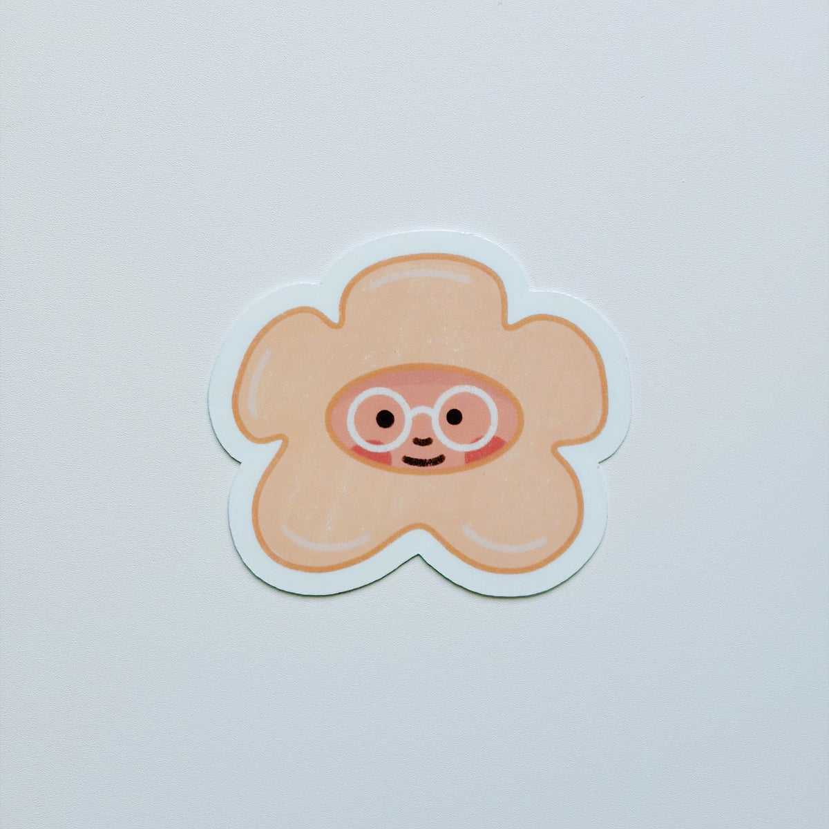 A cute, puakenikeni sticker featuring a smiling face with round glasses, set against a plain light gray background.