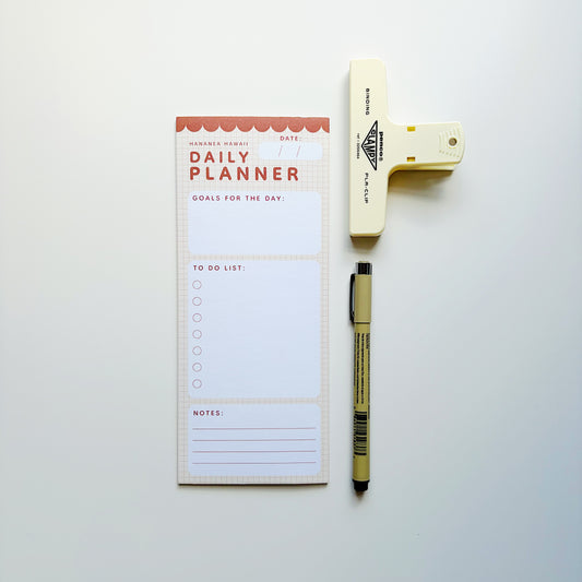 A daily planner notepad with a to-do list and notes section, styled in a flat lay with a beige highlighter and a black pen on a light gray background.