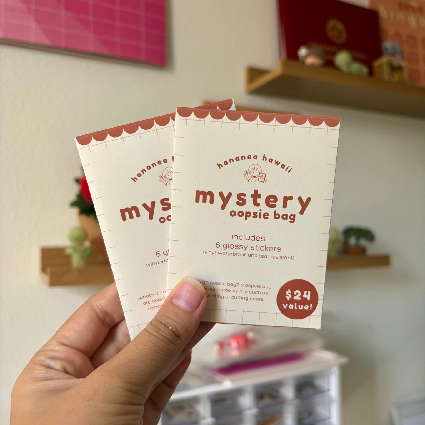 Two 'hananea hawaii' mystery oopsie bag packaging held by a hand with a blurred indoor background.