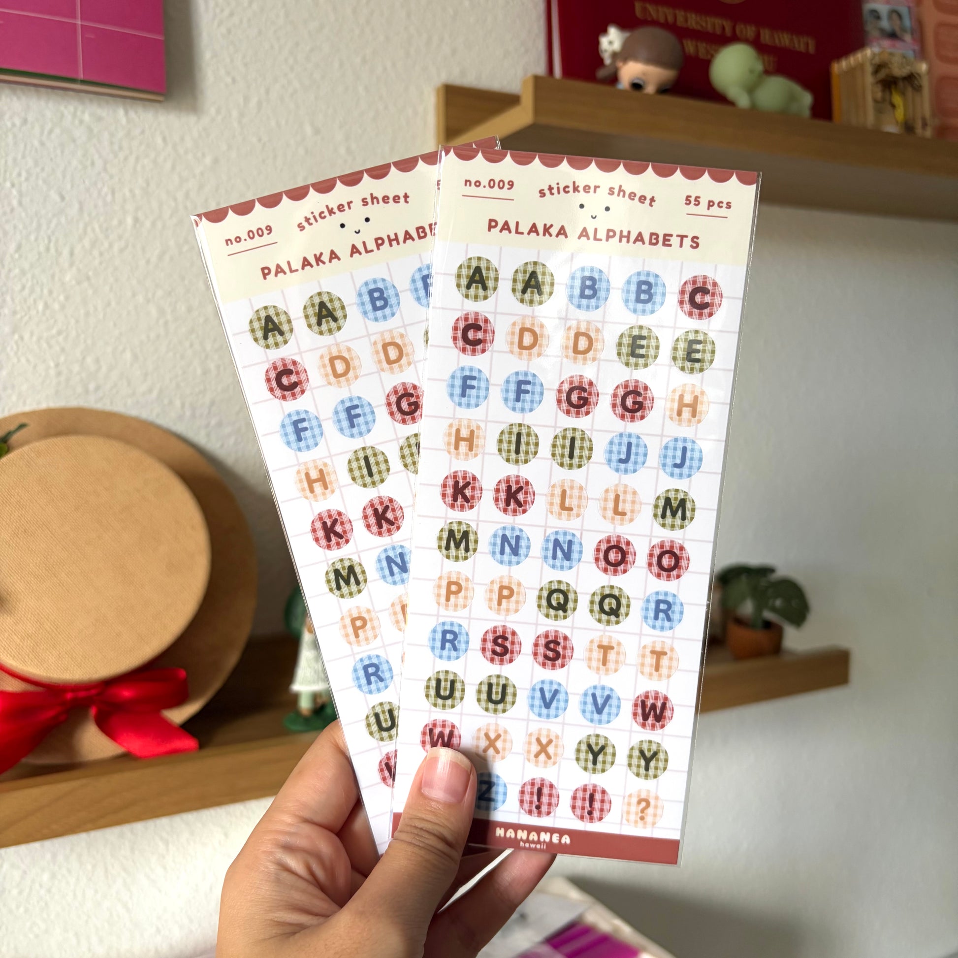 Sheet of colorful alphabet stickers held by a hand with a blurred indoor background.