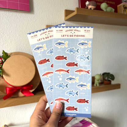 Two sticker sheets with fish designs held by a hand against a home decor background.