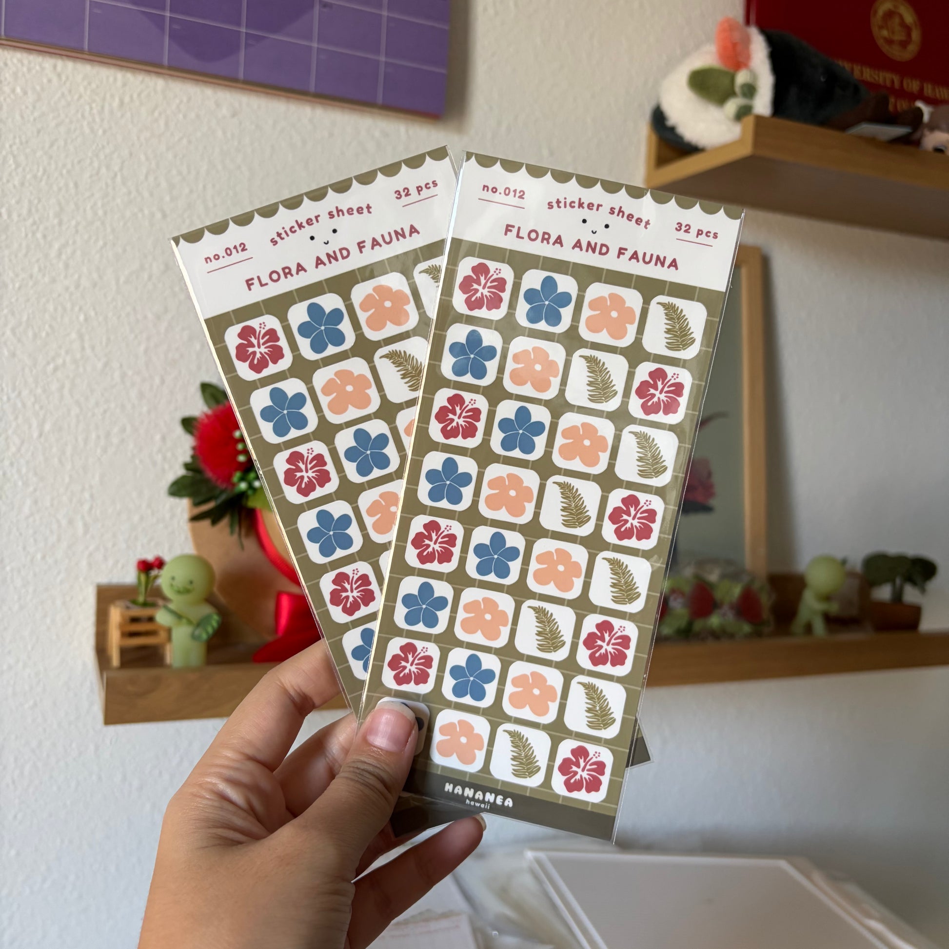 A hand holds two sticker sheets in a home setting.