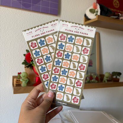 A hand holds two sticker sheets in a home setting.