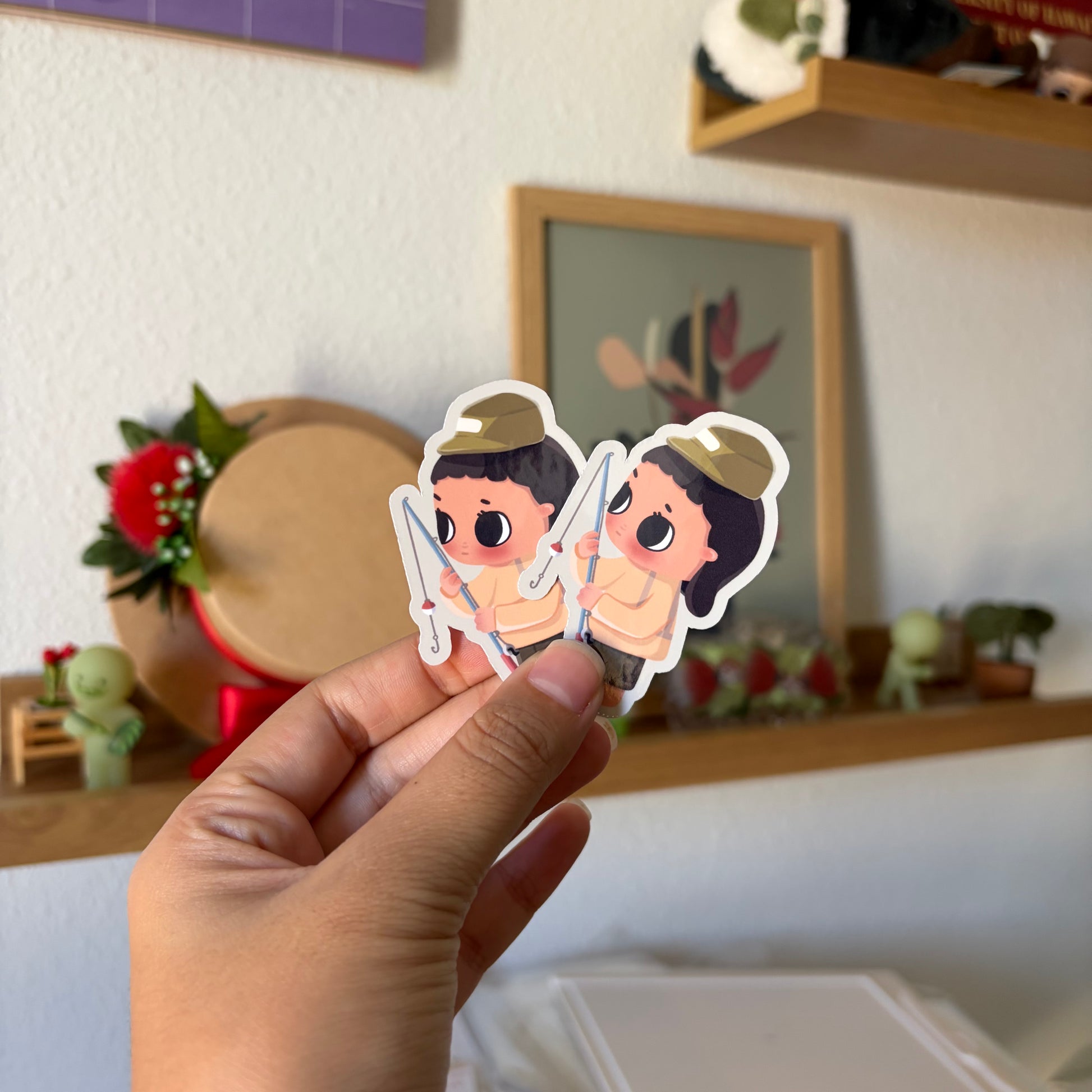 A hand holds two small die-cut stickers featuring cartoon characters.
