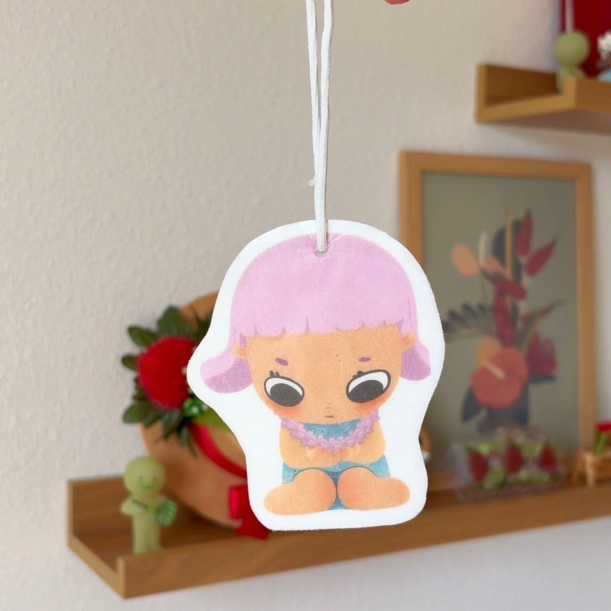 Cartoon character air freshener hanging by a hand with a decorative background