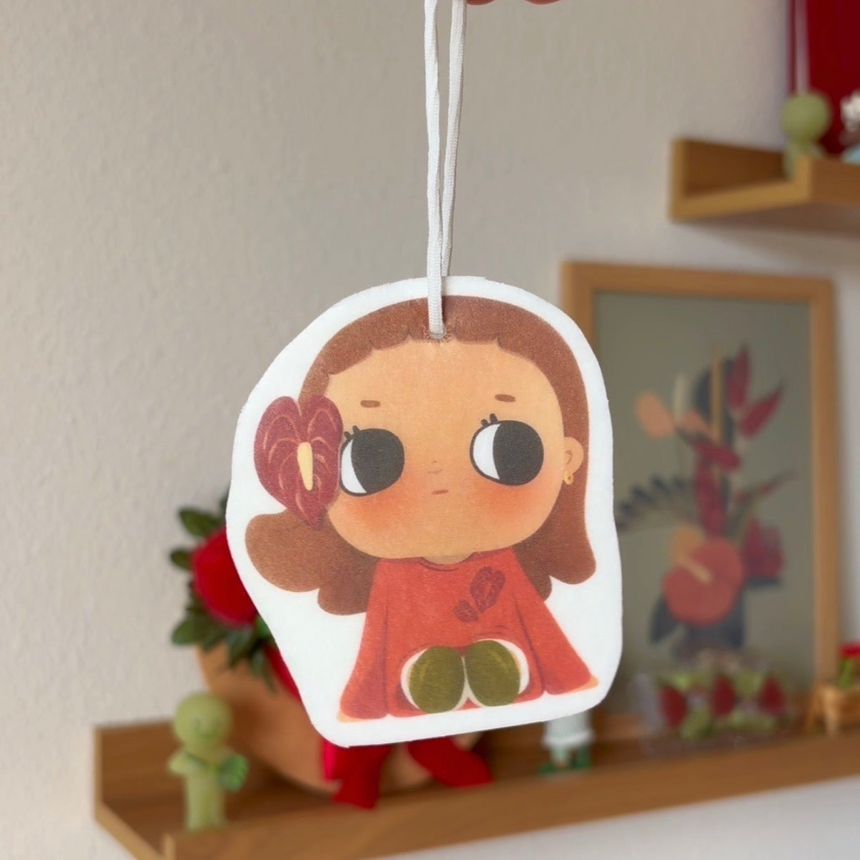Cartoon character air freshener held by a hand with a decorative background