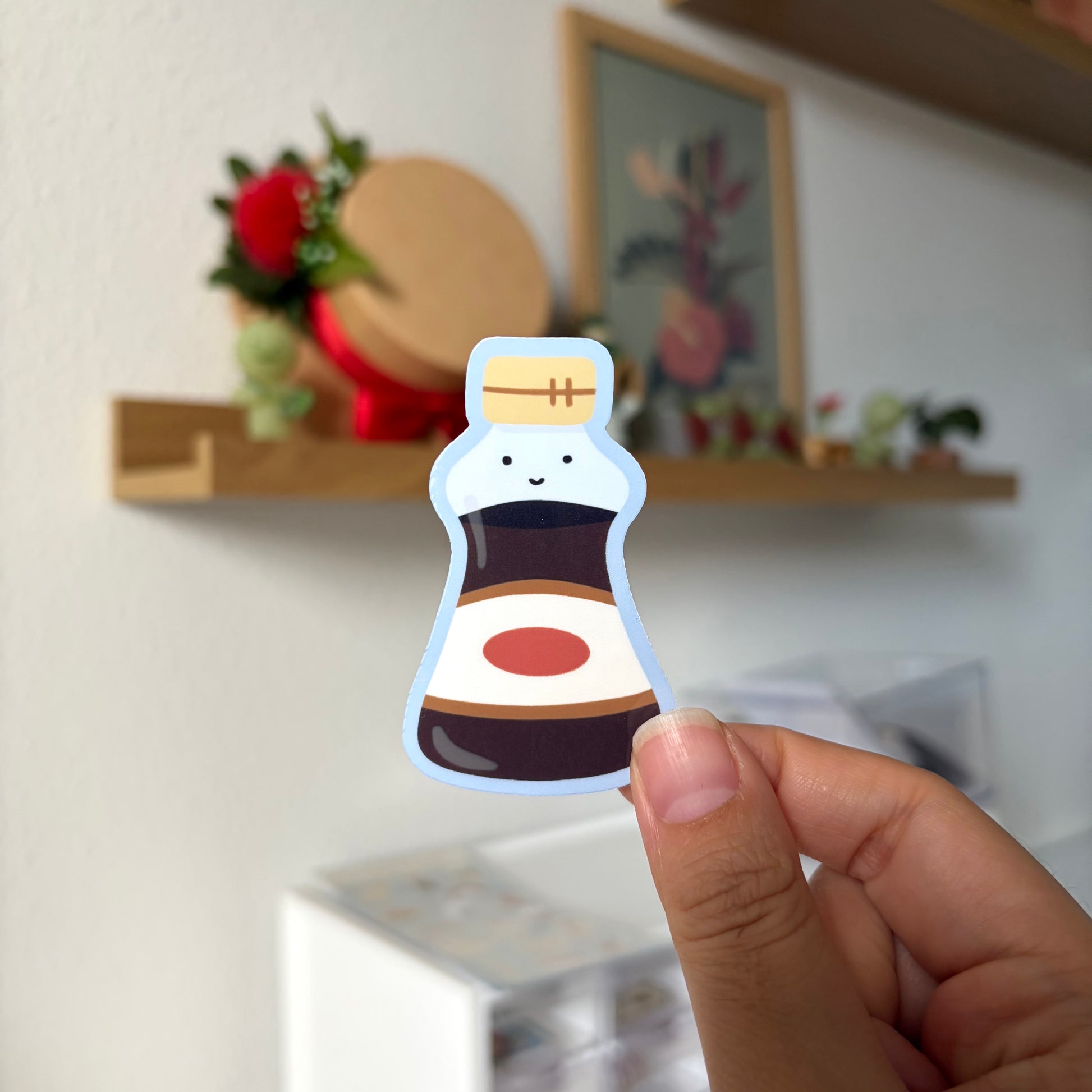 Hand holding a cartoon-style bottle sticker with a blurred indoor background