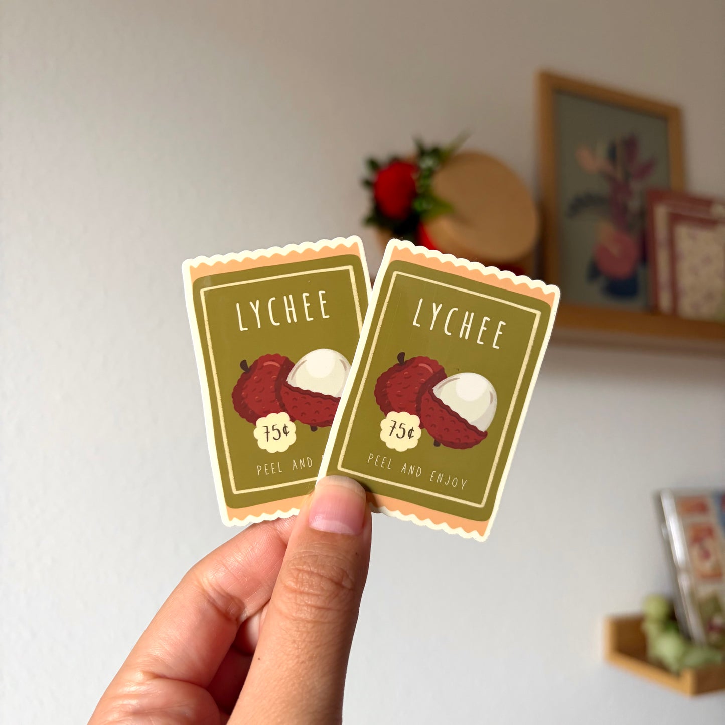 Two lychee-themed stickers held by a hand with a blurred background