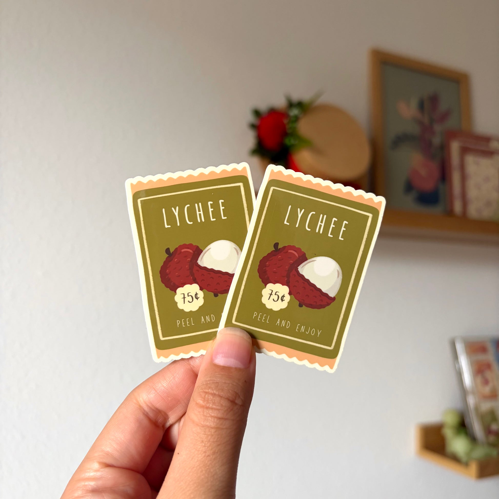 Two lychee-themed stickers held by a hand with a blurred background