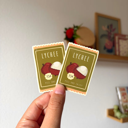 Two lychee-themed stickers held by a hand with a blurred background